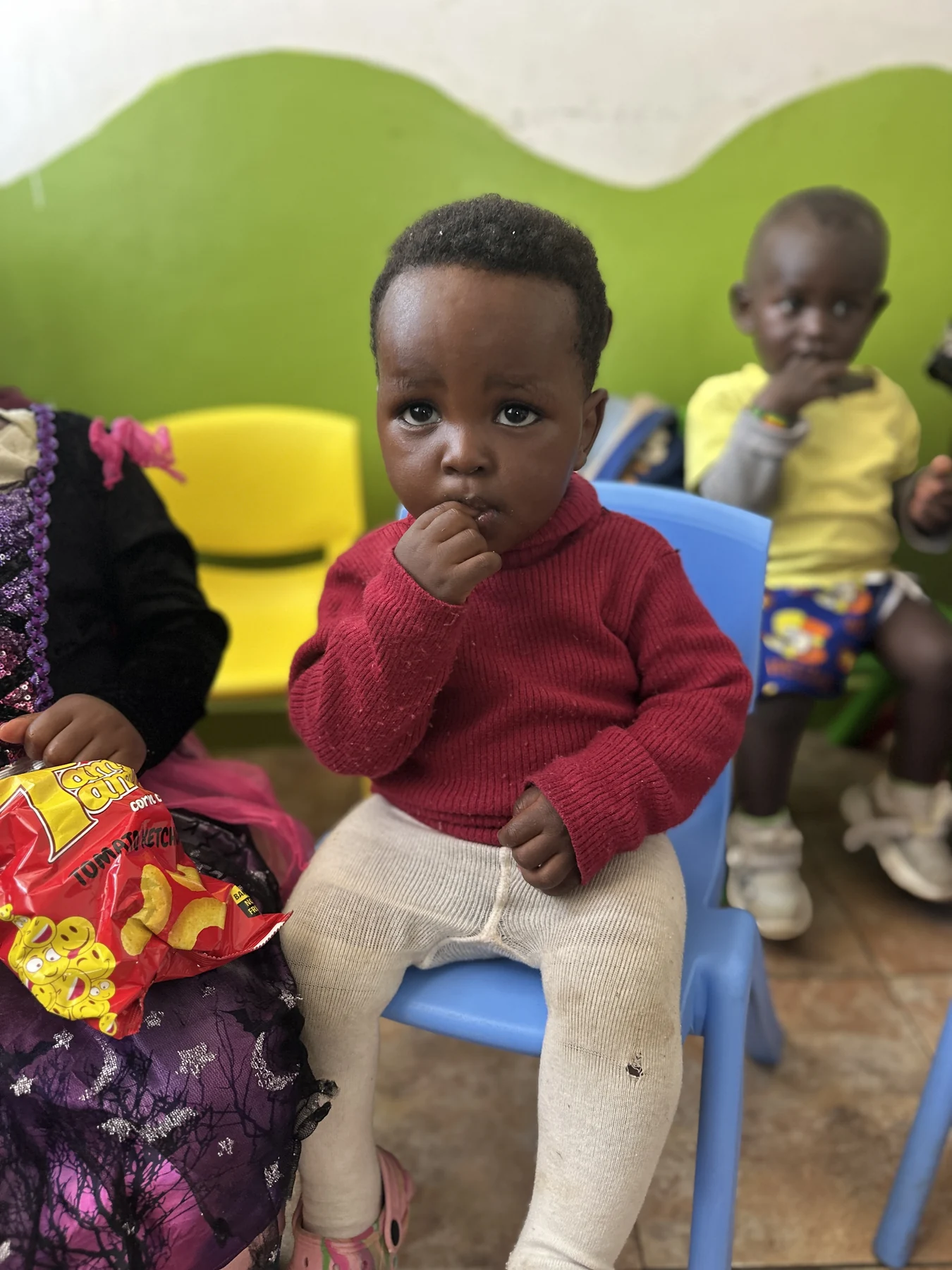 A young child in a red jumper seated among friends at Little Heaven